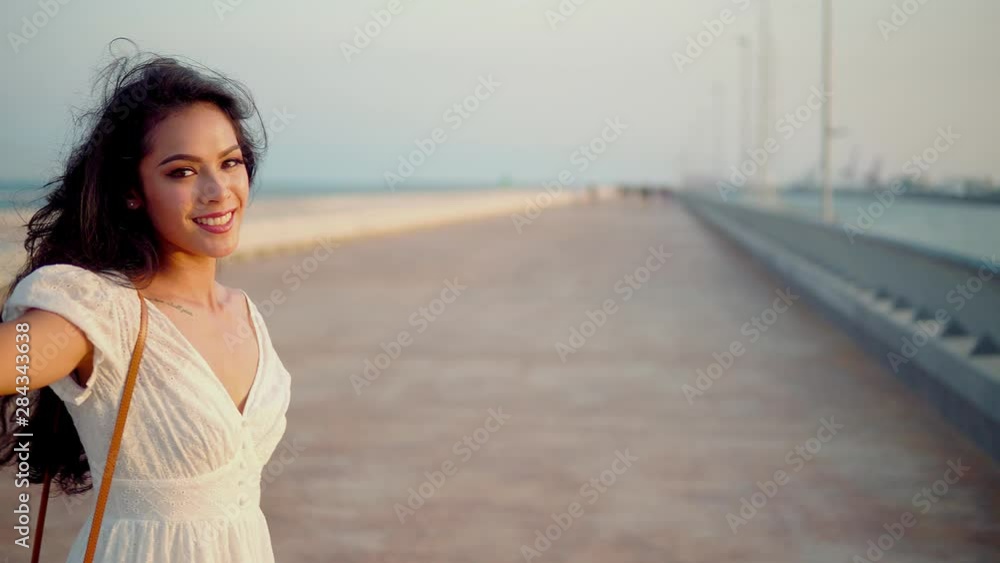 Beautiful girl in the white dress walking along the sea promenade and turning around . Elegance and tenderness concept Beautiful girl in the white dress walking along the sea promenade and turning around . Elegance and tenderness concept