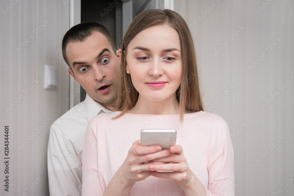 Man peeps into the phone wife, he is shocked by what he saw, girl uses a smartphone, portrait, close up Man peeps into the phone wife, he is shocked by what he saw, girl uses a smartphone, portrait, close up