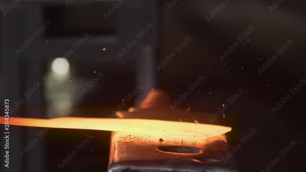 Close-up of a hot yellow glowing knife being forged on an old anvil outside in the darkness of the night - Slow Motion