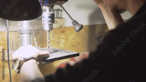 Close over the shoulder shot of knifemaker drilling holes in the blade of a knife with industrial drilling machine in his workshop - Slow Motion photo