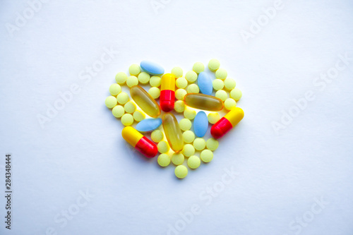 A lot of colorful tablets are laid out in the form of a heart on the background of a white textured rough sheet of paper 