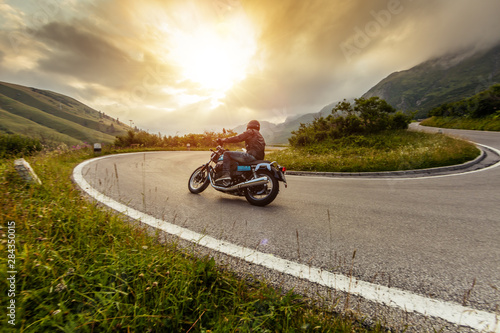 Fotografia Motorcycle driver riding in Alpine landscape.