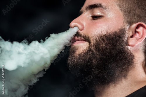 Young caucasian man pull smoke through the nose with a long beard