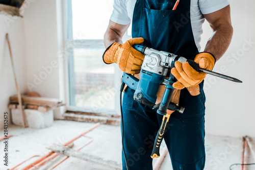 cropped view of workman in yellow gloves holding hammer drill photo