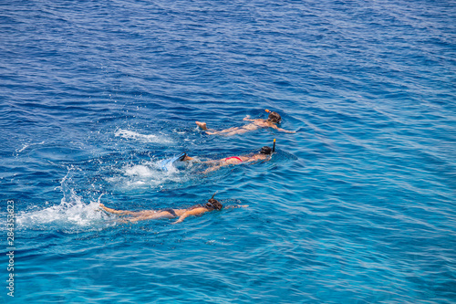 Three young girls snorkeling in blue waters above coral reef on red sea in Sharm El Sheikh, Egypt. People and lifestyle concept. Top view