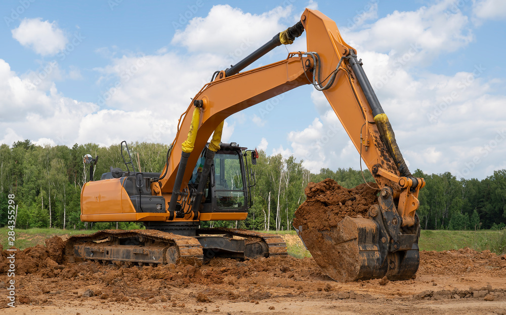 Excavator with a full bucket of clay on the background of the forest. Excavator with a full bucket of clay on the background of the forest.