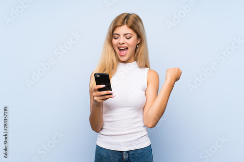 Teenager girl over isolated blue background shouting with mouth wide open to the lateral © luismolinero