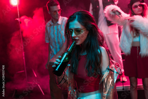 beautiful girl in sunglasses drinking beer in nightclub during rave