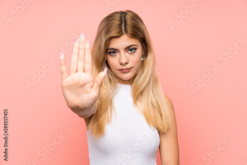 Teenager girl over isolated pink background making stop gesture with her hand