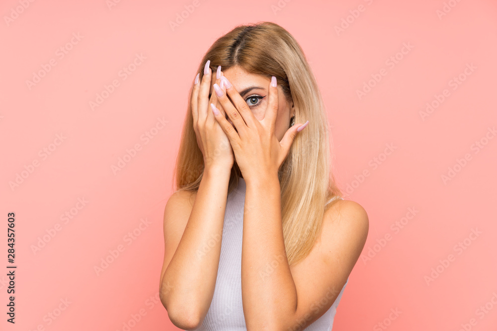 Teenager girl over isolated pink background covering eyes and looking through fingers Teenager girl over isolated pink background covering eyes and looking through fingers