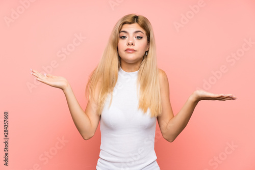 Teenager girl over isolated pink background having doubts with confuse face expression