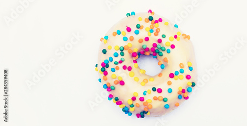 Yellow donut with bright sprinkles on a white background, copy space, advertising
