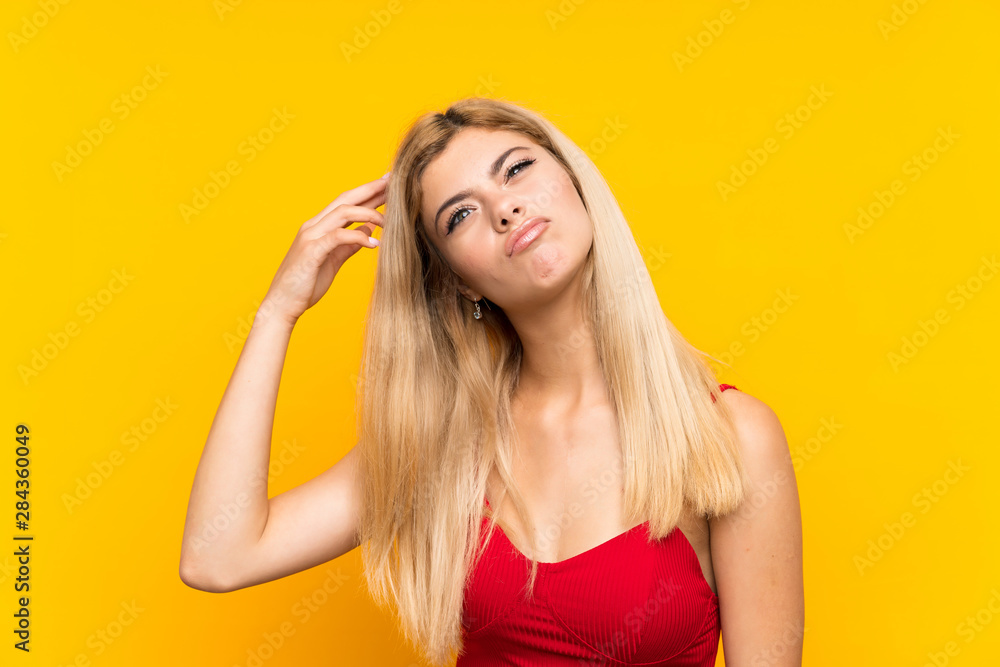 Teenager girl over isolated yellow background having doubts and with confuse face expression