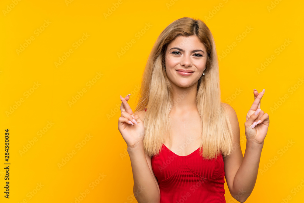 Teenager girl over isolated yellow background with fingers crossing Teenager girl over isolated yellow background with fingers crossing