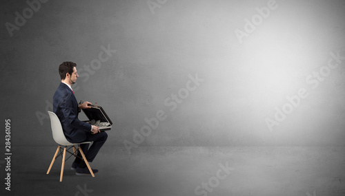 Tablou pe pânză Businessman staying in an empty grey dark room with stuffs on his lap