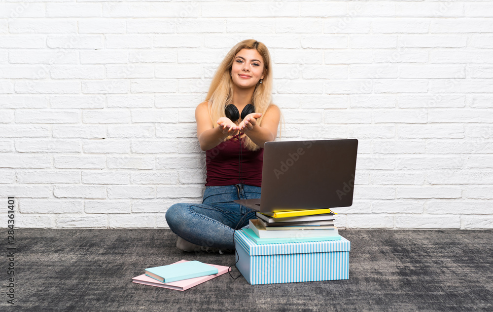 Teenager girl sitting on the floor with her laptop holding copyspace imaginary on the palm to insert an ad Teenager girl sitting on the floor with her laptop holding copyspace imaginary on the palm to insert an ad