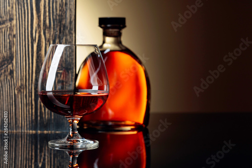 Glass and bottle of brandy on a black reflective background.
