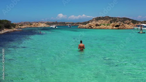 Young Man walking in water in La Spiaggia di Santa Maria beach in La Maddalena archipelago, Sardinia, Italy