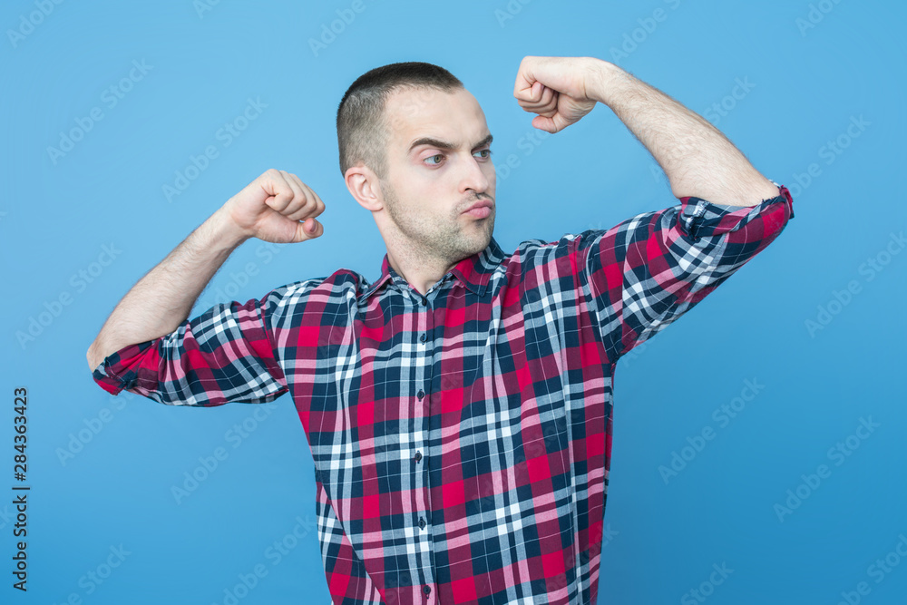 Portrait, narcissistic young guy shows his strength, front view, blue background, Portrait, narcissistic young guy shows his strength, front view, blue background,