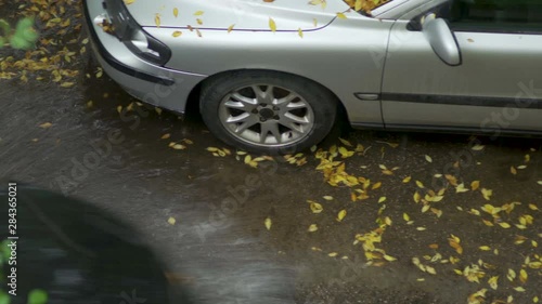 A car rides through puddles past a standing car. Puddle on the pavement on a rainy autumn day. View from above. Pan to right camera mowement photo