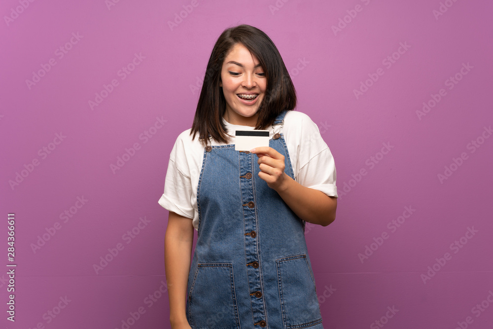 Young Mexican woman over isolated background holding a credit card Young Mexican woman over isolated background holding a credit card