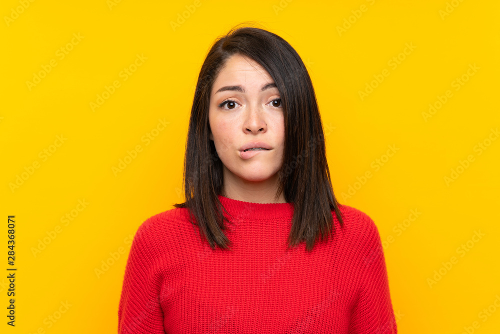 Young Mexican woman with red sweater over yellow wall having doubts and with confuse face expression Young Mexican woman with red sweater over yellow wall having doubts and with confuse face expression
