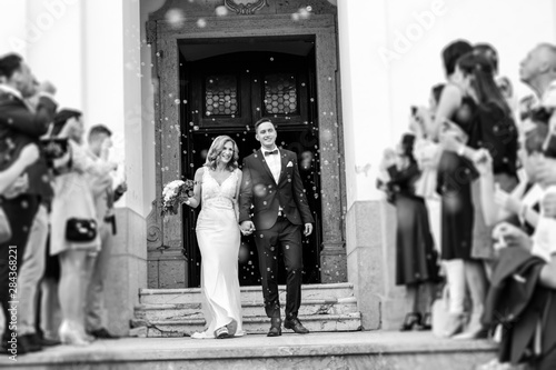 Quadro su tela Newlyweds exiting the church after the wedding ceremony, family and friends celebrating their love with the shower of soap bubbles, custom undermining traditional rice bath