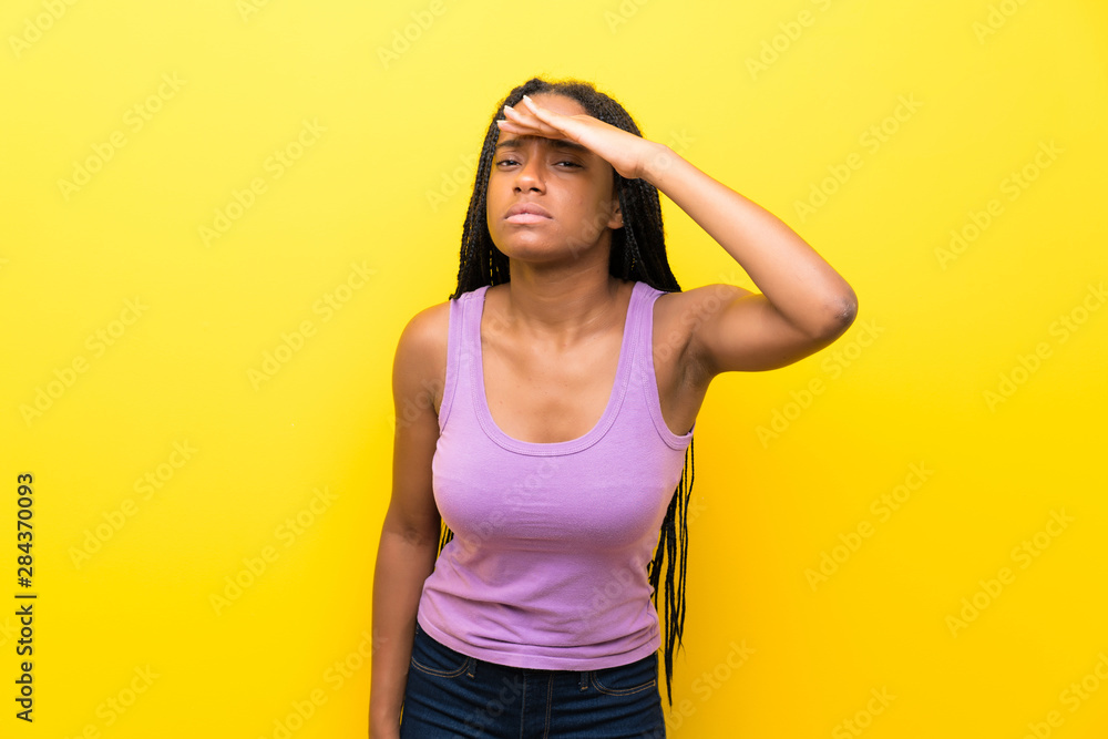 African American teenager girl with long braided hair over isolated yellow wall looking far away with hand to look something African American teenager girl with long braided hair over isolated yellow wall looking far away with hand to look something