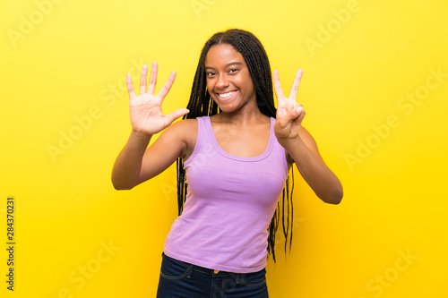 African American teenager girl with long braided hair over isolated yellow wall counting seven with fingers