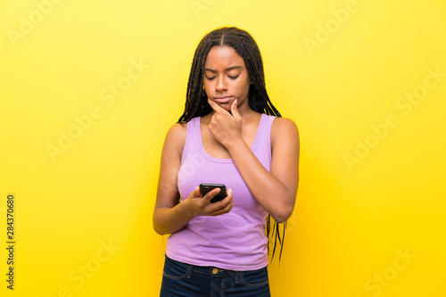 African American teenager girl with long braided hair over isolated yellow wall thinking and sending a message
