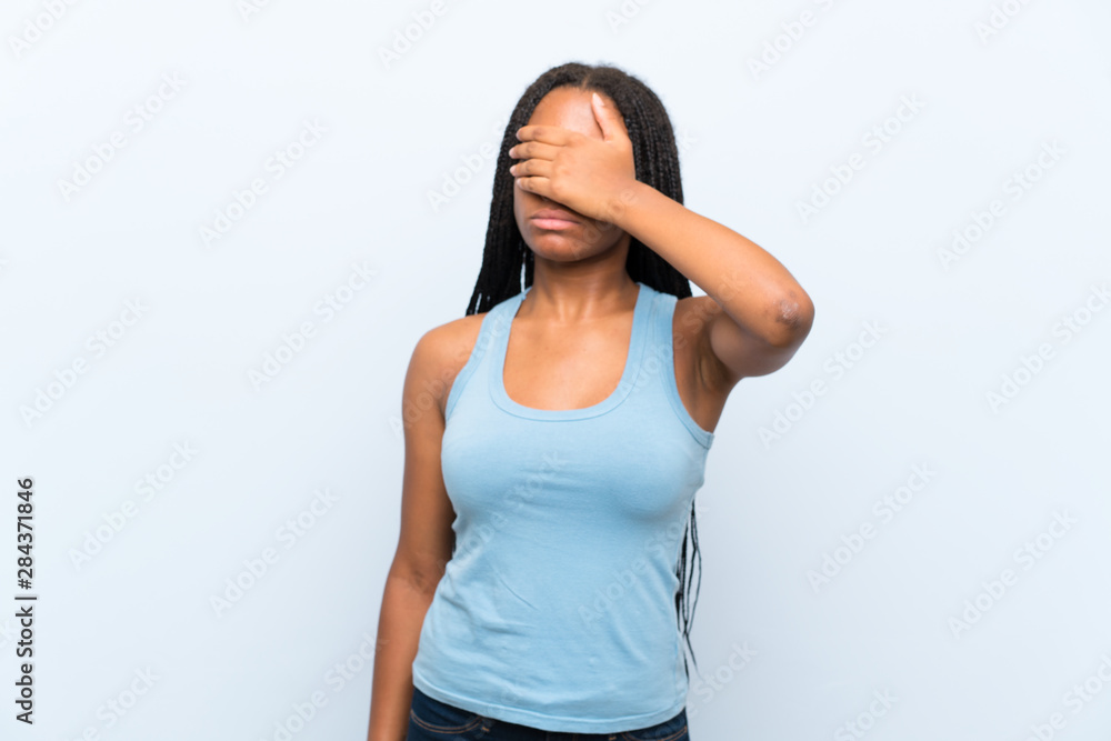 African American teenager girl with long braided hair over isolated blue background covering eyes by hands African American teenager girl with long braided hair over isolated blue background covering eyes by hands
