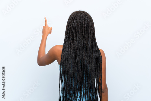 African American teenager girl with long braided hair over isolated blue background pointing back with the index finger photo