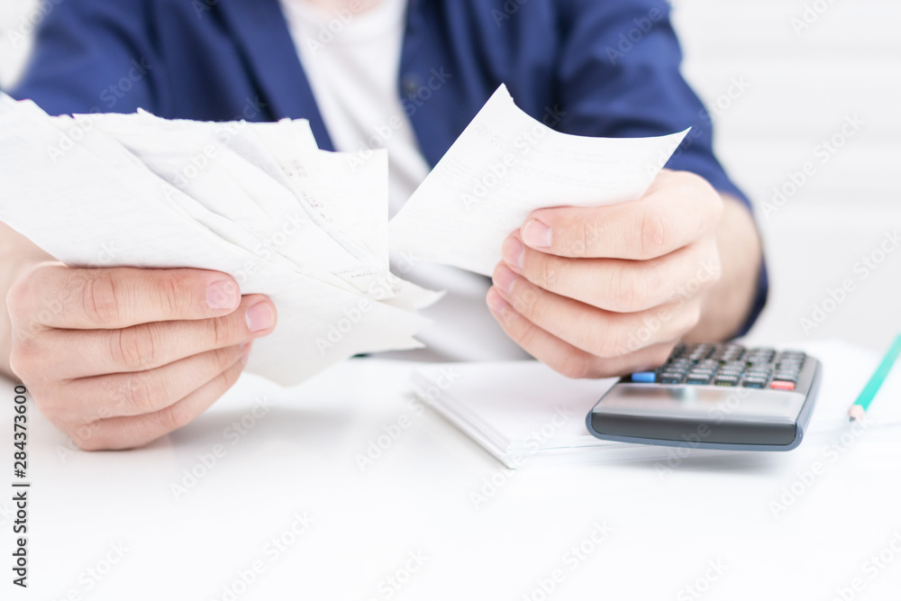 Man holding papers in her hands, calculating family budget, calculator on the desktop, men's hands, cropped image, close up Man holding papers in her hands, calculating family budget, calculator on the desktop, men's hands, cropped image, close up