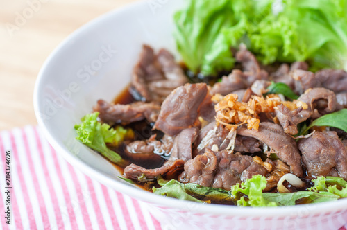 Chinese premium beef noodle with green lettuce topping with roasted garlic in white bowl on wooden table.