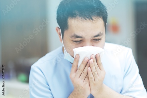 Asian man blowing nose and sneezing into white tissue paper