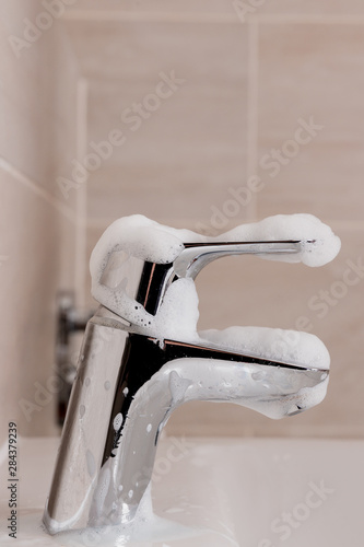 Shiny tap in bathroom. Bubbles and foam from cleaning products. Housekeeping and maid in bathroom.