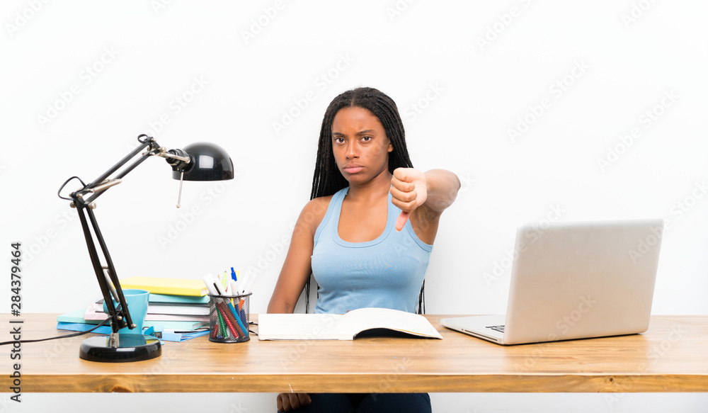 African American teenager student girl with long braided hair in her workplace showing thumb down with negative expression African American teenager student girl with long braided hair in her workplace showing thumb down with negative expression