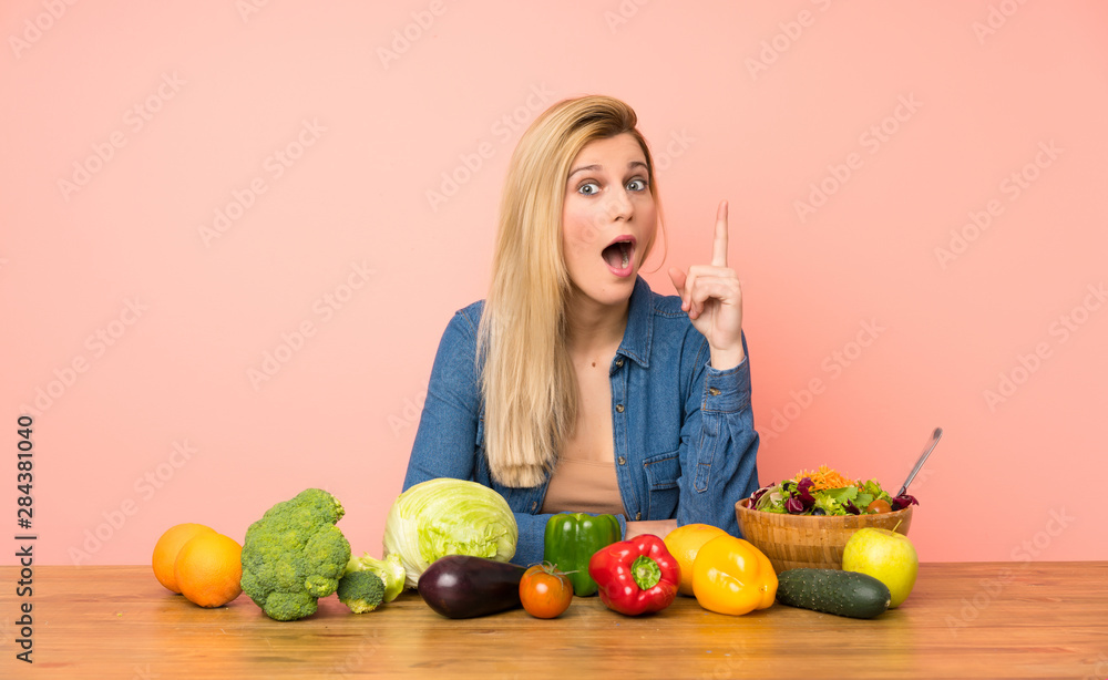 Young blonde woman with many vegetables thinking an idea pointing the finger up Young blonde woman with many vegetables thinking an idea pointing the finger up