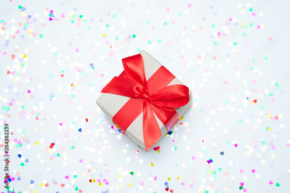 White desk with scattered sparkles hearts, gift box with red ribbon, close up, top view, the concept of the holidays White desk with scattered sparkles hearts, gift box with red ribbon, close up, top view, the concept of the holidays