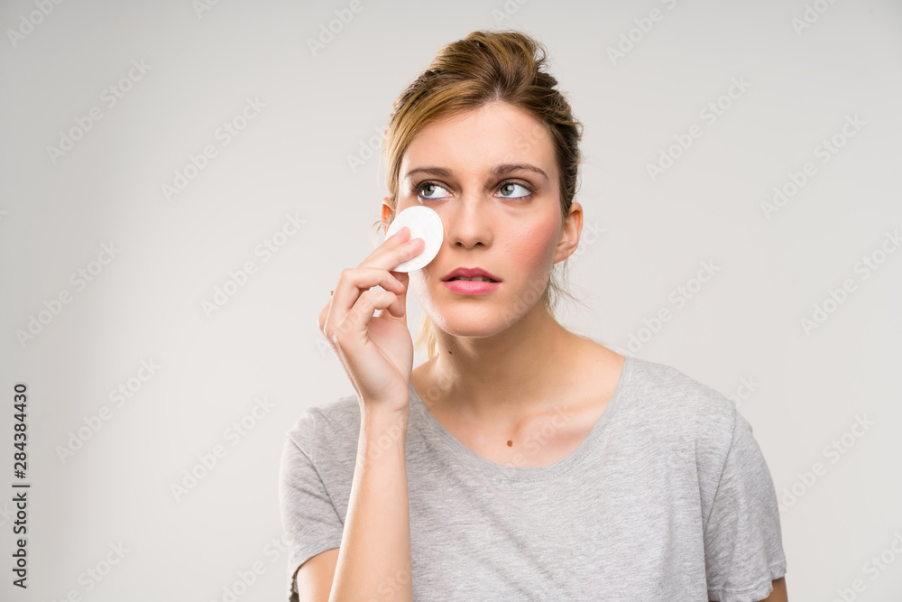 Young blonde woman removing makeup from her face with cotton pad Young blonde woman removing makeup from her face with cotton pad