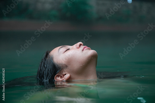 Traveler woman enjoying a spa day in natural hot springs - Hispanic young woman Submerged Up To Her Face in Water with eyes closed
