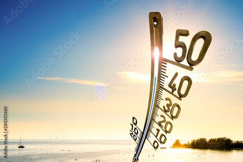 Hintergrund für einen heißen Sommertag oder eine Hitzewelle, Strand mit Menschen, strahlender Sonne und ein großes Thermometer photo