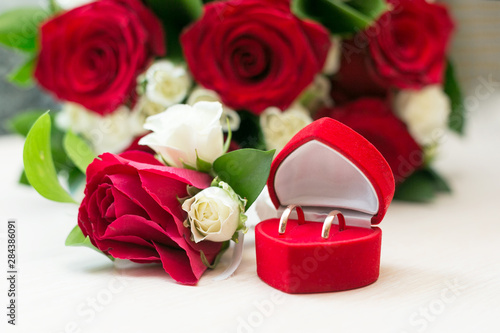 Wedding rings on a background of a bouquet of roses. A box with wedding rings on a table next to a beautiful bouquet of white and red roses.