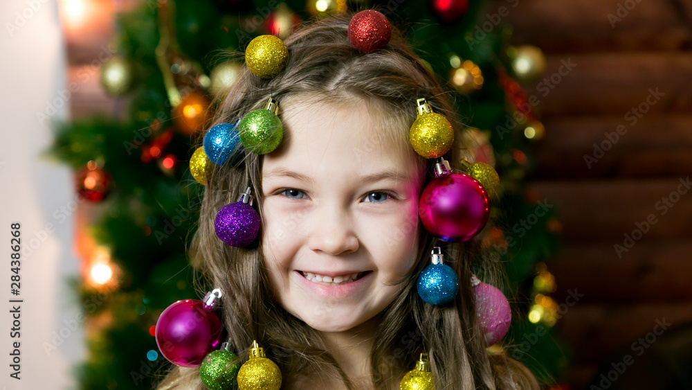 Little girl with garlands holiday balls woven into her hair with Christmas decorations. Girl with Christmas decorations on her head. Little girl with garlands holiday balls woven into her hair with Christmas decorations. Girl with Christmas decorations on her head.