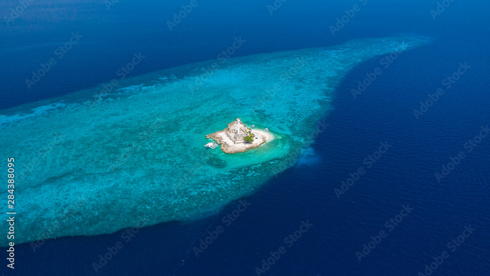 Aerial drone view of tropical Capitancillo Island in the Philippines showing its lighthouse and coral reef