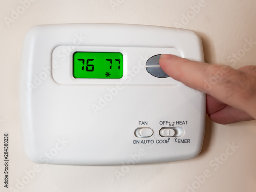Closeup of a man's hand setting the room temperature on a programmable home thermostat.