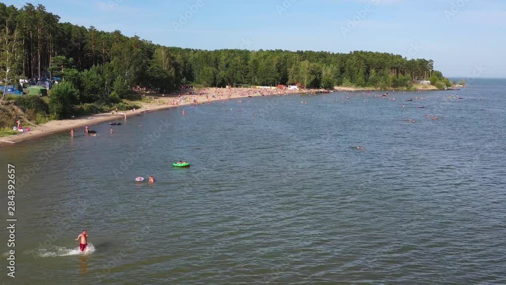 Top view of the beach, featuring colorful umbrellas and people relaxing on a summer day. Hot day, many people sunbathe and swim Top view of the beach, featuring colorful umbrellas and people relaxing on a summer day. Hot day, many people sunbathe and swim