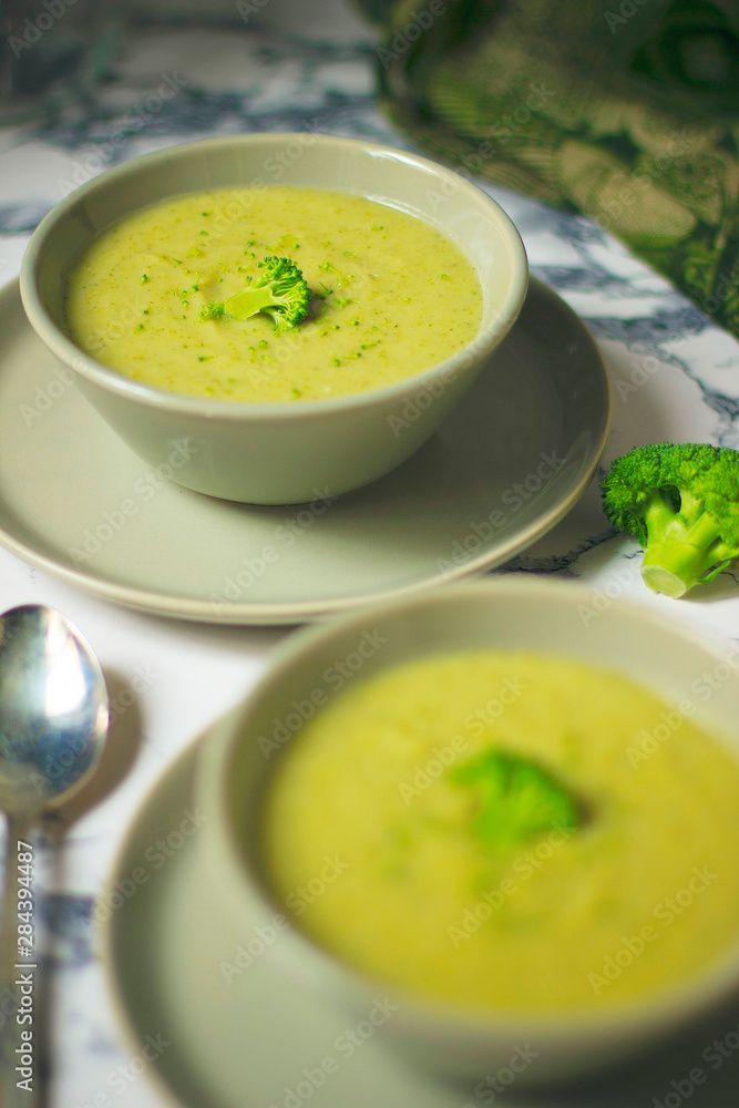 Fresh Broccoli cream soup on two gray ceramic bowl on plate with spoon on marble background,vegetarian food,healthy concept