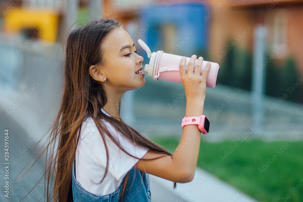 Portrait of young small girl drinking water from thermos, on hands smart watches. Portrait of young small girl drinking water from thermos, on hands smart watches.