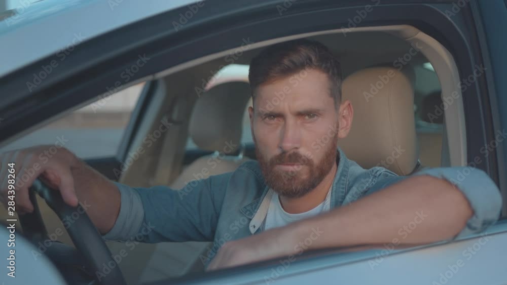 Male portrait of confident driver hands on wheel sitting in the car at sunset. Handsome young bearded man driving his auto in downtown. Male portrait of confident driver hands on wheel sitting in the car at sunset. Handsome young bearded man driving his auto in downtown.